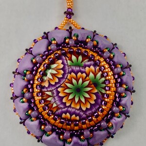 May include: A purple and orange beaded pendant with a floral design. The pendant is made with small beads and has a loop at the top for hanging.