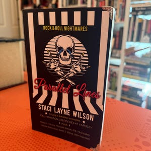 May include: A hardcover book titled "Parallel Lines" by Staci Layne Wilson. The cover features a skull with lightning bolt eyes, crossed bones, and the text "Rock & Roll Nightmares." The book has a black and white striped design with silver corner protectors.