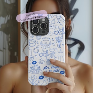 May include: White phone case with blue doodle illustrations of wedding-related icons. The case includes the text "Magsafe Custom Name & Date" and "Mrs. Hayes 10.25 2026". The design features hearts, cakes, and a car.