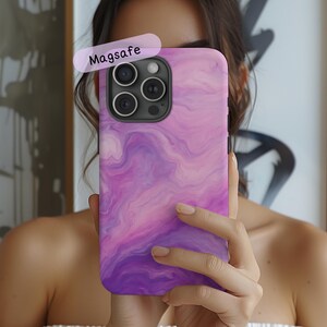May include: A smartphone case featuring a swirling purple and pink marble pattern with a black camera cutout. The case includes a label with the text Magsafe. The design covers the entire back of the phone case with a smooth, fluid aesthetic.