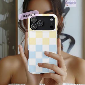 May include: A phone case with a checkerboard pattern in pastel yellow, light blue, and white. The case has a black camera module and the word "Magsafe" is printed on a label. The brand name "Cozyria" is visible in the upper right corner.