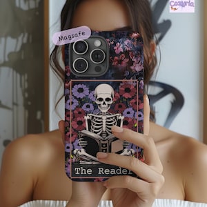 May include: A phone case with a floral design and a skeleton reading a book. The case has a dark background with pink and purple flowers. The text "The Reader" is at the bottom of the case.