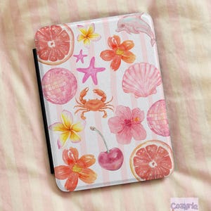 May include: A rectangular e-reader case featuring a white background with vertical light pink stripes. The surface is decorated with watercolor illustrations of pink grapefruit slices, orange and yellow flowers, a pink starfish, a crab, a seashell, a dolphin, two disco balls, and a cherry.