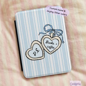 May include: A light blue and white striped book cover with a heart-shaped locket design. The locket has the words "Books + coffee" and the initials "P.E." The cover has a blue ribbon and the text "Custom name & saying. Other colors".