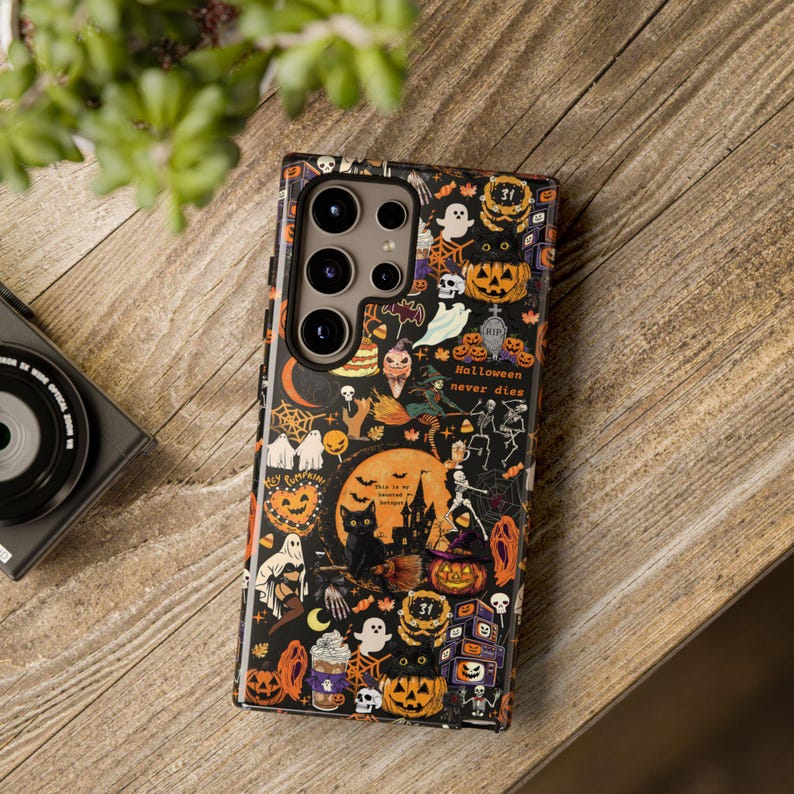 May include: A rectangular smartphone case featuring a black background with a dense pattern of orange, white, and purple Halloween-themed illustrations including pumpkins, ghosts, skeletons, cats, and the text "Halloween never dies".