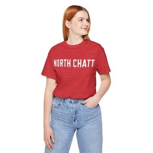 May include: A red t-shirt with white text that says "NORTH CHATT" on the front. The shirt is made of a soft, comfortable material.