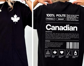 May include: Black t-shirt with a white maple leaf graphic on the front. The back of the shirt features the text "100% POLITE CANADIAN" with a description and warning about Canadian culture. The shirt is a casual wear item.