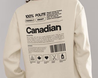 May include: Beige sweatshirt with a graphic print of a Canadian flag and text that reads "100% Polite, Friendly, Smart, Canadian". The text describes Canadians as maple-syrup-fueled, winter-surviving superheroes who can turn "eh" into an entire conversation.