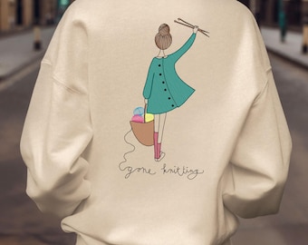 May include: A beige sweatshirt with a graphic of a woman holding yarn and knitting needles. The text "gone knitting" is printed below the graphic.