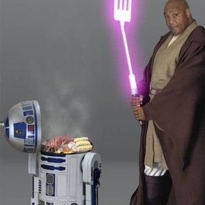 Peut inclure: Image humoristique d'une personne en robe Jedi tenant une spatule violette lumineuse. Un barbecue en forme de R2-D2 est ouvert, avec de la nourriture en train de cuire. Le thème mélange Star Wars et le barbecue.