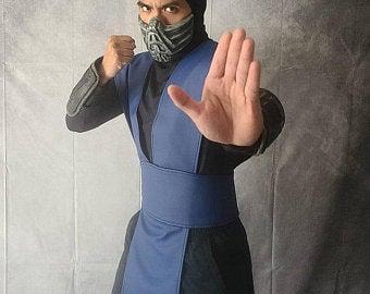 Puede incluir: Una persona con un disfraz de ninja azul y negro con una máscara. El disfraz incluye una túnica azul, cinturón y protectores de brazos. La persona está haciendo un gesto con la mano.