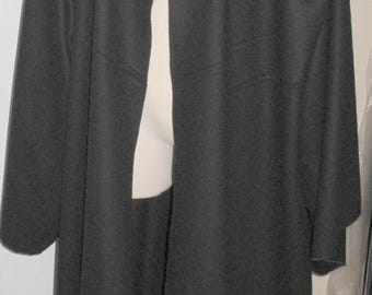 May include: A long, black hooded cloak on a mannequin. The cloak features a wide collar and long sleeves, extending to the floor. The fabric looks to be a heavy, opaque material.