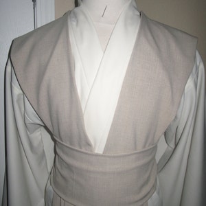 Pu&ograve; includere: Un costume beige chiaro e bianco esposto su un manichino. Il costume presenta un cappotto beige con un ampio colletto e una cintura abbinata. Lo strato inferiore &egrave; bianco, con maniche lunghe. Il costume &egrave; progettato con uno scollo a V.