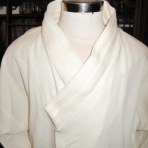 May include: A white, long-sleeved robe with a wide, folded collar. The robe is made of a lightweight fabric and has a simple, elegant design.