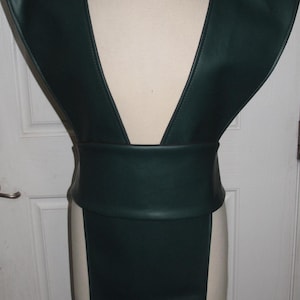 Könnte beinhalten: Eine dunkelgrüne Kunstlederweste mit tiefem V-Ausschnitt und einem breiten Gürtel. Die Weste hat einen langen, fließenden Rock.