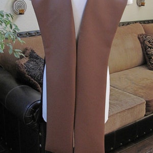 May include: A brown leather waistcoat with a V-neckline, displayed on a mannequin against a white wall. The waistcoat is on a silver stand with wheels.