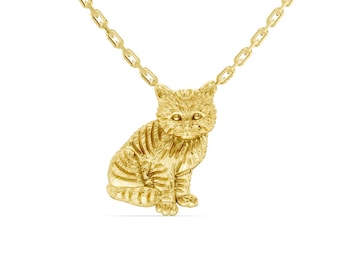 May include: A gold-colored cat pendant necklace. The pendant is a detailed, three-dimensional sculpture of a sitting cat with striped markings. The necklace chain is also gold-colored and has a delicate link design.