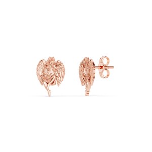 May include: A pair of rose gold angel stud earrings. Each earring features a detailed depiction of an angel with outstretched wings. The earrings are set against a white background.