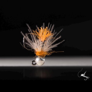 Puede incluir: Un pequeño señuelo de pesca con mosca naranja y blanco con cabeza de cuentas.