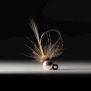 May include: A small, silver and red fly fishing lure with a brown and green body and a white feather tail.
