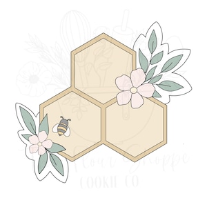 May include: A cookie cutter in the shape of a honeycomb with a bee and floral accents. The honeycomb is beige, with a small bee in the center. Pink flowers and green leaves are on the sides.