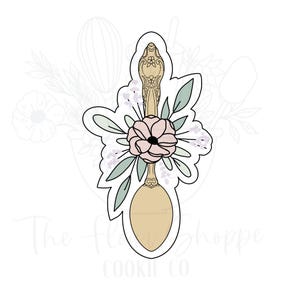 May include: A cookie cutter in the shape of a spoon, decorated with a floral arrangement. The spoon has an ornate handle and a light tan bowl. The floral arrangement includes a pink flower, green leaves, and small white flowers. The text "The Flowe Shoppe Cookie Co" is at the bottom.