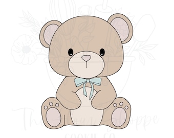 May include: A cookie cutter in the shape of a teddy bear. The bear is light brown with a light blue bow. The bear has black eyes and a small nose. The cookie cutter is for making cookies.