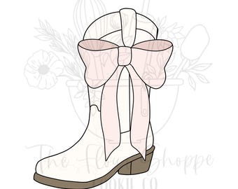 May include: A white cowboy boot cookie cutter with a light pink bow. The boot has a brown heel and sole. The background features a floral design and the text "The Flower Shoppe Cookie Co."