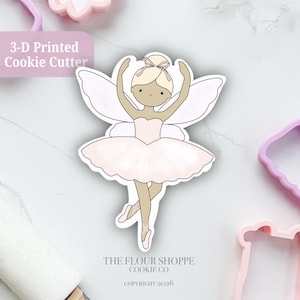 May include: A 3-D printed cookie cutter shaped like a fairy ballerina with wings, wearing a light pink tutu and ballet slippers. The design features a tan-skinned figure with blonde hair in a bun, arms raised, and the text 3-D Printed Cookie Cutter.