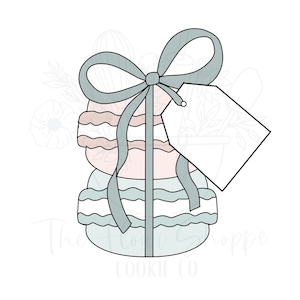 May include: A blue and white cookie cutter shaped like a stack of macarons with a blue ribbon and a blank tag. The cookie cutter is perfect for making macaron cookies.