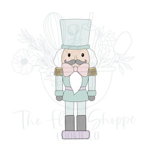 May include: A light blue and white nutcracker cookie cutter with a pink bow and a white beard. The cookie cutter is standing on a purple base with the text "The Flour Shoppe Cookie Co."
