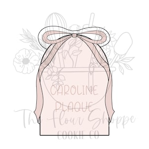 May include: A light pink cookie cutter in the shape of a gift bag with a bow. The text "Caroline Plaque Flour Shoppe Cookie Co" is written on the gift bag. The background has a floral design.