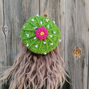 May include: A green crocheted hat shaped like a cactus with a pink and yellow flower in the center.