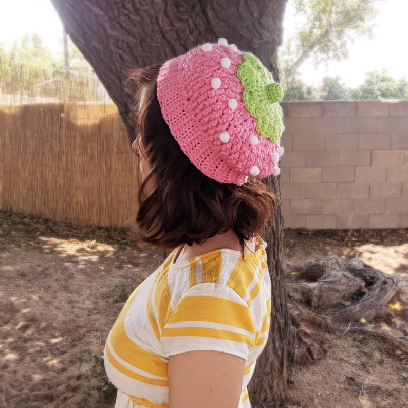 May include: A pink and green crocheted strawberry hat with white pom-poms.