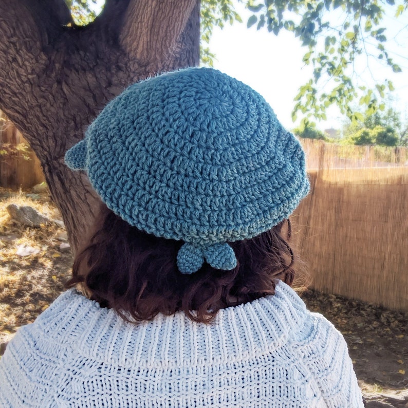 Pu&ograve; includere: Un berretto di lana blu chiaro con un design unico che presenta due piccole forme arrotondate sul retro. Il berretto &egrave; indossato da una persona con i capelli lunghi e scuri.
