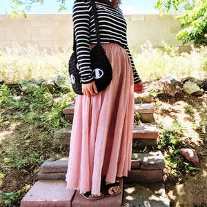 May include: A woman wearing a black and white striped long-sleeved shirt and a long pink skirt. She is carrying a black crocheted bag with white eyes.