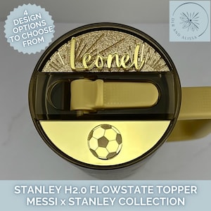 Pu&ograve; includere: Un coperchio superiore per bicchiere Stanley H2.0 FlowState color oro con una targhetta personalizzata che riporta il nome Leonel in corsivo dorato, un emblema di pallone da calcio dorato e un meccanismo di chiusura scorrevole scuro.