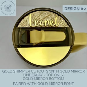 May include: A circular tumbler lid featuring a gold shimmer top section with the name Leonel in gold mirror script font. The lid includes a dark translucent sliding closure and a solid gold mirror bottom section. Text reads DESIGN #2.