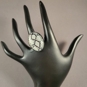 May include: A black and white oval ring with a snakeskin pattern.