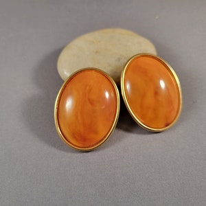 May include: A pair of oval-shaped orange clip-on earrings with gold-toned metal settings.