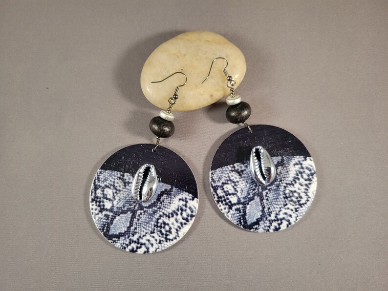 These big, statement earrings feature large, round snake-print wood pendants accented with gunmetal gray painted cowrie shells, black and metallic silver colored wood and gunmetal gray-plated brass beads.