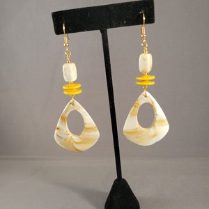 May include: A pair of gold dangle earrings with a white and brown marbled triangle-shaped pendant and yellow beads.