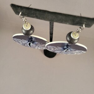 May include: A pair of dangle earrings with a black and white patterned design. The earrings feature a black and white bead with a white centre.