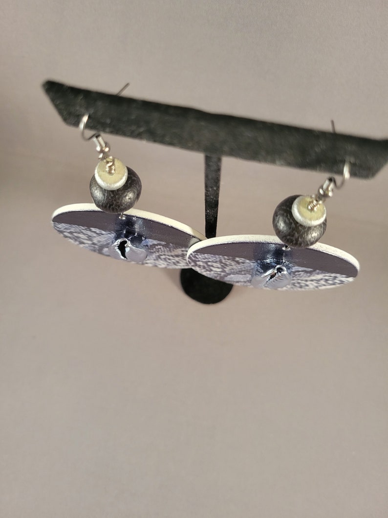 May include: A pair of dangle earrings with a black and white patterned design. The earrings feature a black and white bead with a white centre.