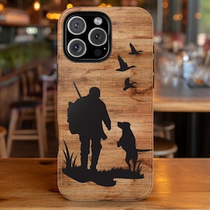 May include: A wood-grain iPhone case with a silhouette of a hunter and a dog, with flying birds in the background.