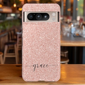 May include: A pink glitter phone case with a black camera cutout and the word "grace" written in cursive.