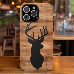May include: A wooden-textured phone case featuring a black silhouette of a deer. The case has a natural wood grain appearance and is designed to fit a smartphone, with cutouts for the camera and buttons.
