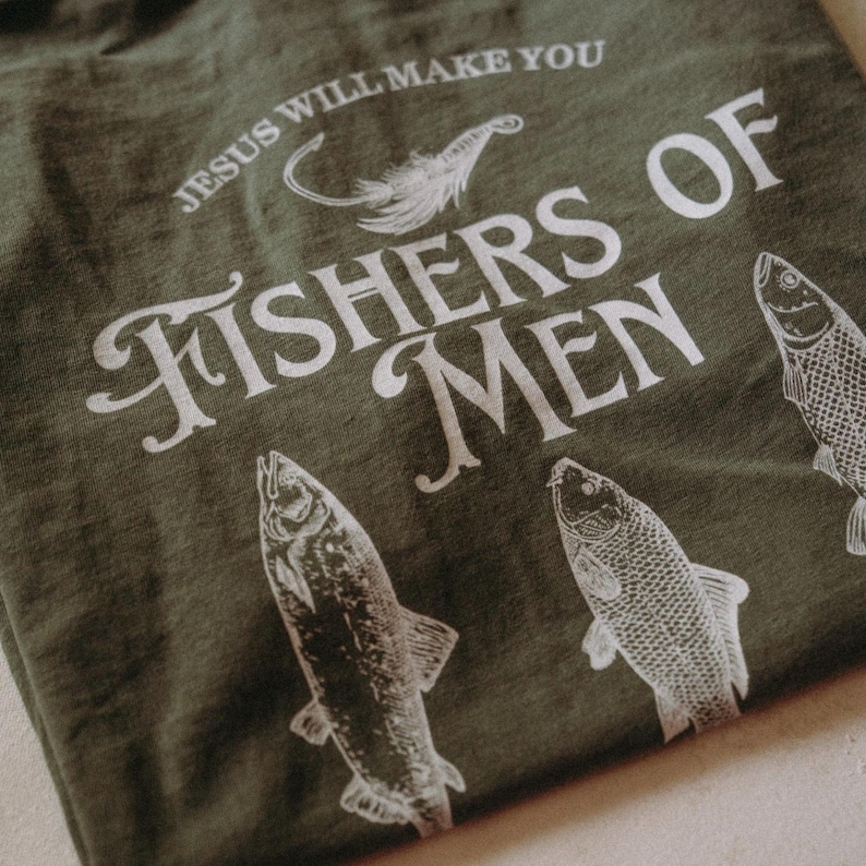 May include: Olive green t-shirt with the text "JESUS WILL MAKE YOU FISHERS OF MEN" in white. The shirt features a graphic of a fishing lure and three fish illustrations.