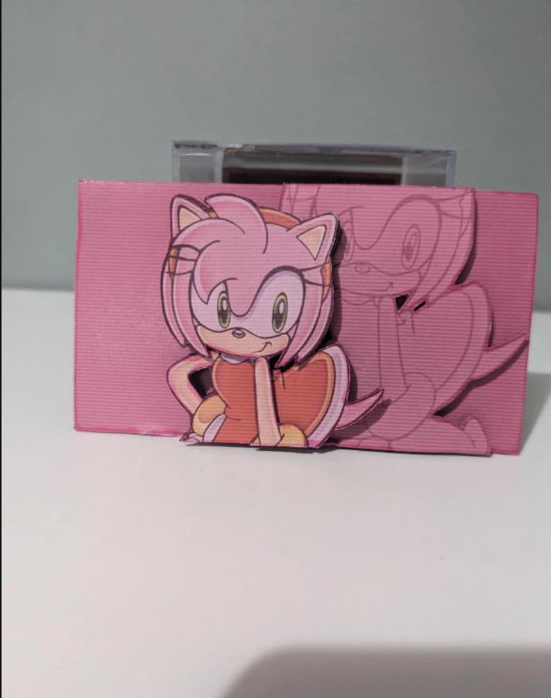 May include: A pink and white cardboard box with a cutout of a pink cartoon character with a red dress and pink hair. The character is holding a heart in her hand. The box has a clear plastic window on the top.