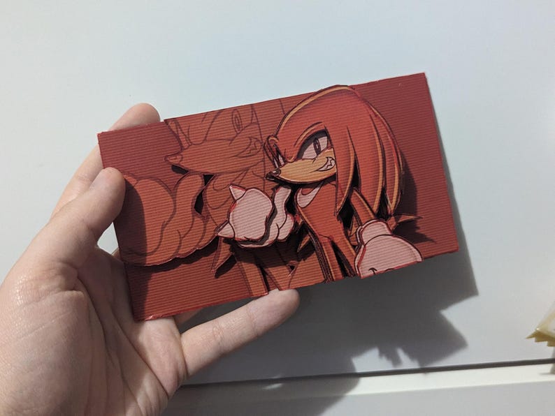May include: A 3D printed red and orange papercraft of Knuckles the Echidna from the Sonic the Hedgehog video game series. The papercraft is a detailed and intricate representation of the character, with a textured surface and a layered design.
